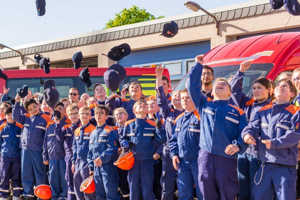 Kinder und Jugendliche der Jugendfeuerwehr Lehrte werfen vor der Feuerwache ihre Mützen in die Luft